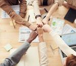 Top view of a diverse team fist bumping over a meeting table with paperwork and laptops, symbolizing teamwork.