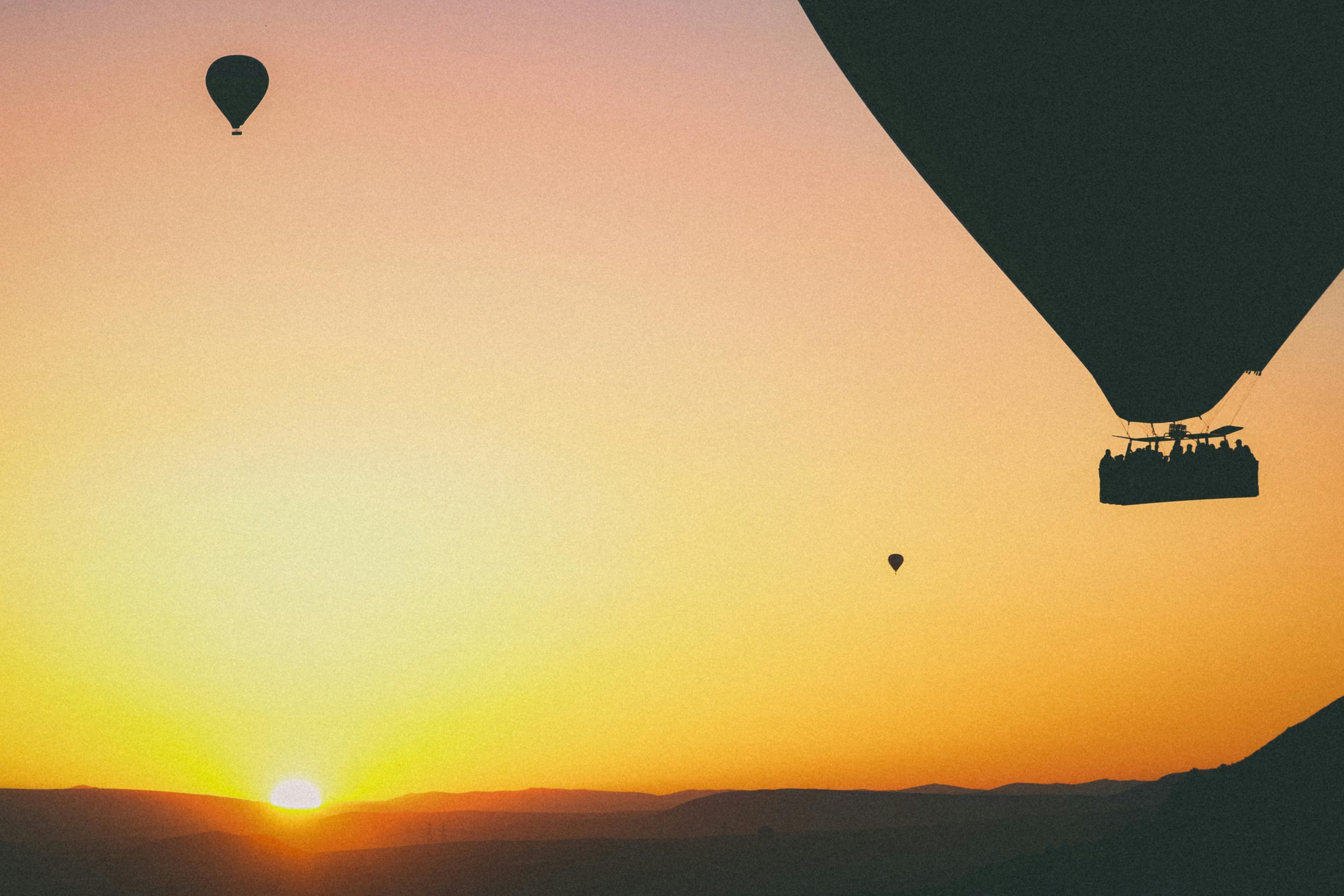 Silhouettes of hot air balloons flying across a vibrant sunset sky, creating a serene and adventurous scene.